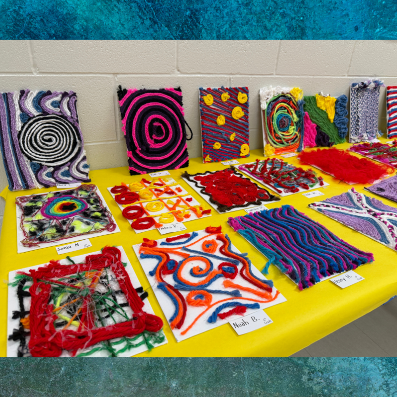 A display of colorful yarn art projects on a yellow tablecloth.