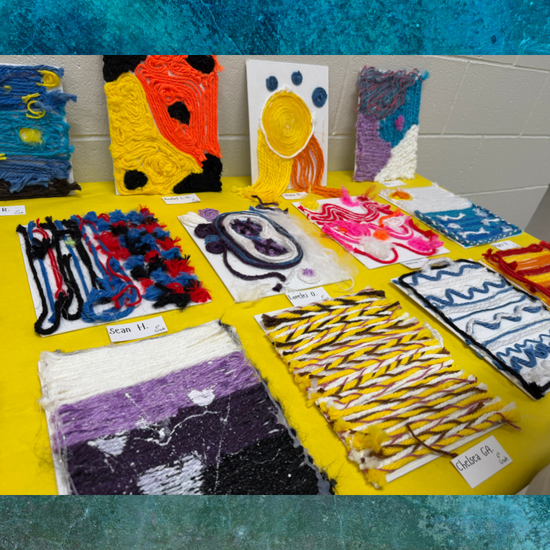 A display of colorful woven art pieces made from yarn on a yellow tablecloth.