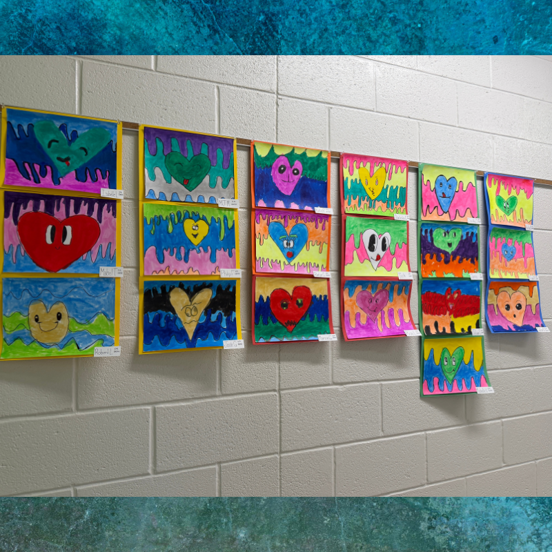 A wall display of colorful, hand-drawn heart artworks, each with unique faces and vibrant backgrounds.