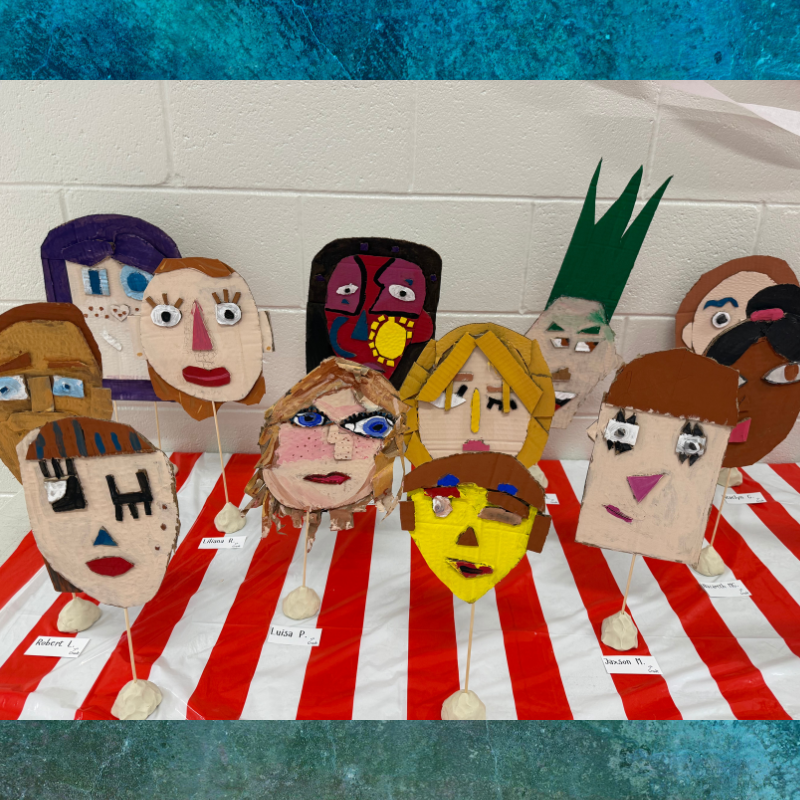 A collection of colorful, handmade cardboard masks with unique facial features displayed on sticks.
