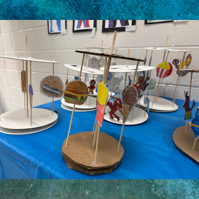 A display of handmade carousel models featuring drawings of food items like burgers, fries, and ice cream.