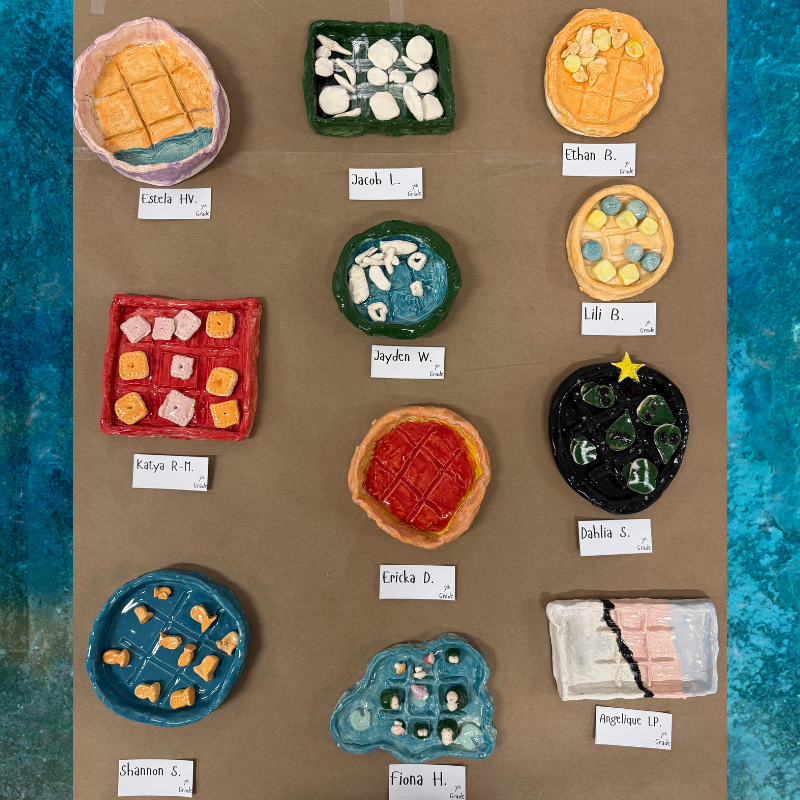 A display of colorful, handmade ceramic art pieces, resembling food items like waffles and pizza.