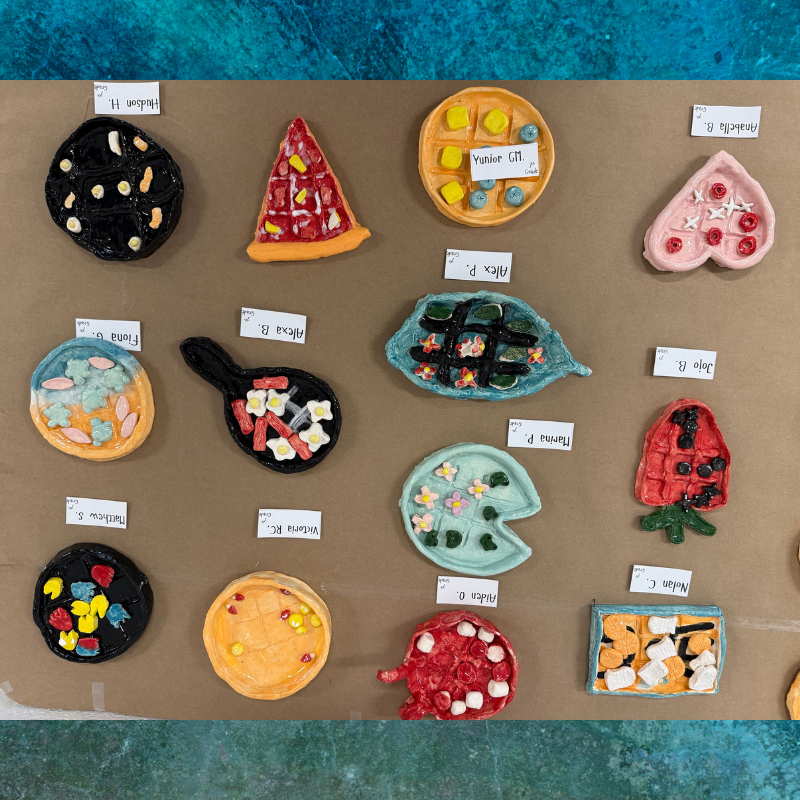 A display of colorful, handmade clay creations resembling food items like waffles, pizza, and sushi.