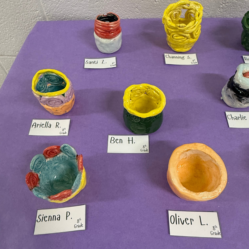 A display of colorful, handmade ceramic bowls and vases created by 8th-grade students.