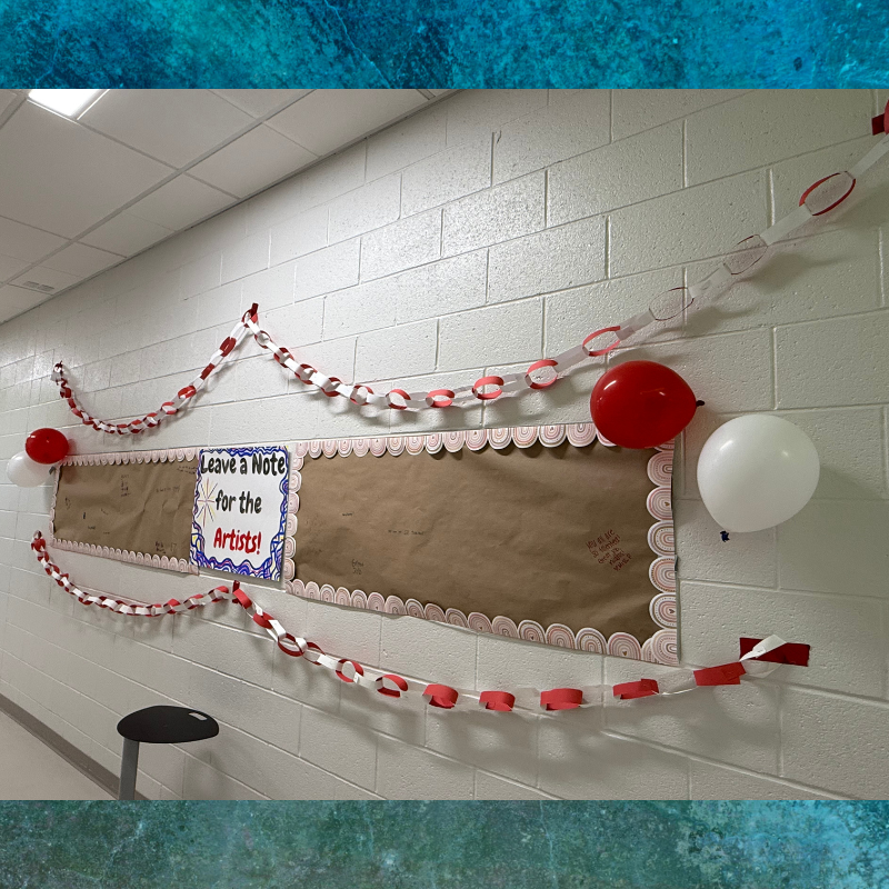 A bulletin board in a hallway decorated with red and white paper chains and balloons.