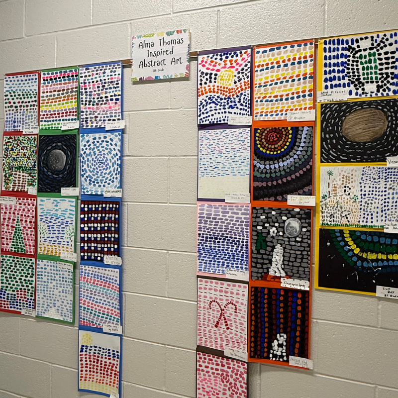 A wall display showcases numerous colorful abstract art pieces inspired by Alma Thomas, created by students.