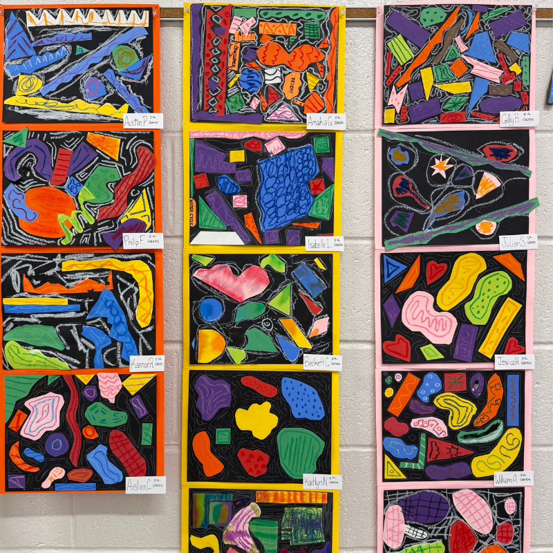 A wall display of colorful, abstract art pieces created by students, each with a name tag.