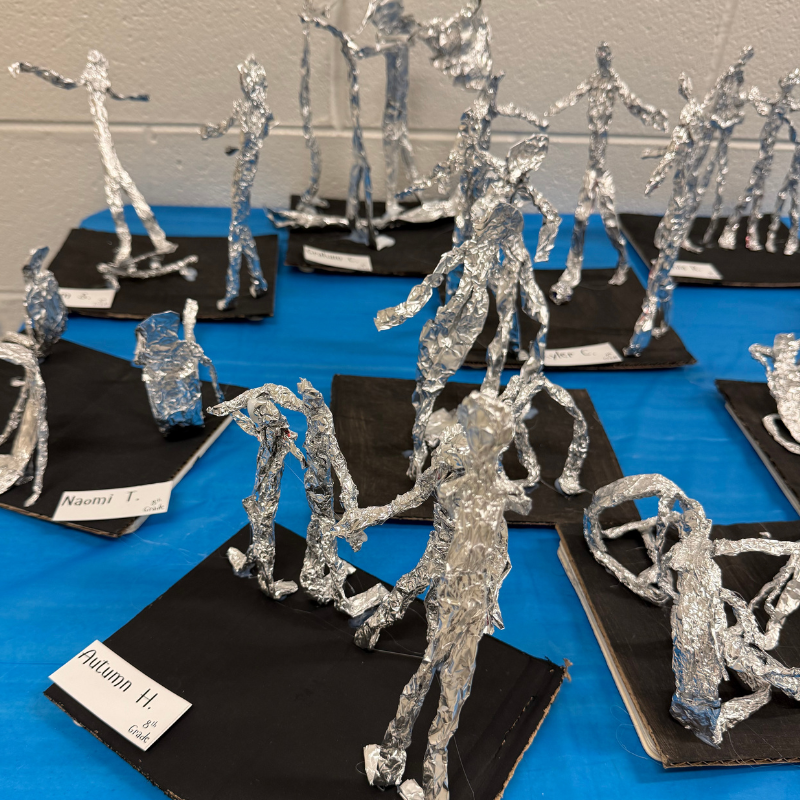 A collection of foil sculptures depicting human figures in various poses, displayed on a blue tablecloth.