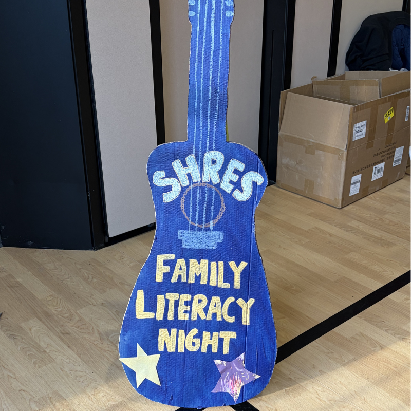 A blue cardboard guitar cutout with 'SHRES FAMILY LITERACY NIGHT' written on it.
