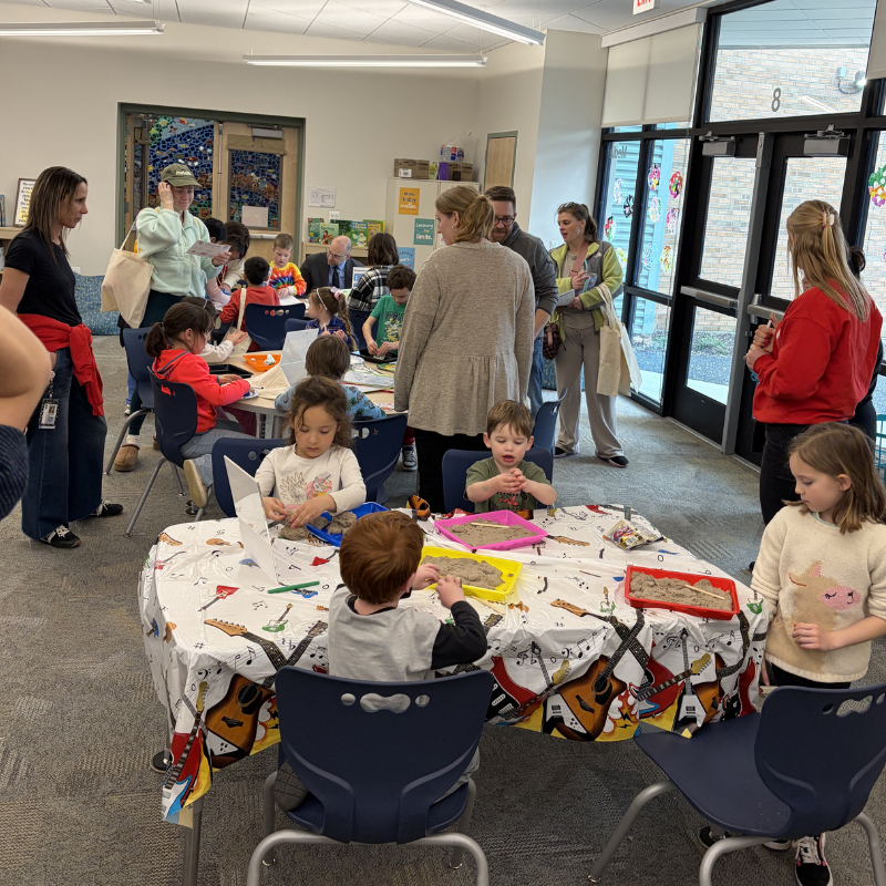 Children engage in sensory play with sand at tables decorated with musical instruments.