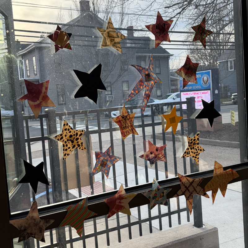 A window decorated with various handmade paper stars of different patterns and colors.