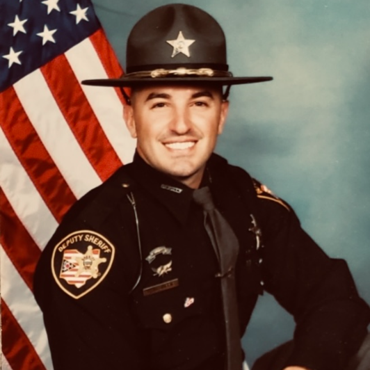 A smiling Deputy McDuffie in uniform poses in front of an American flag.