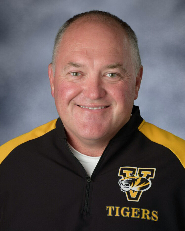A smiling man wearing a black and yellow jacket with the word TIGERS visible.