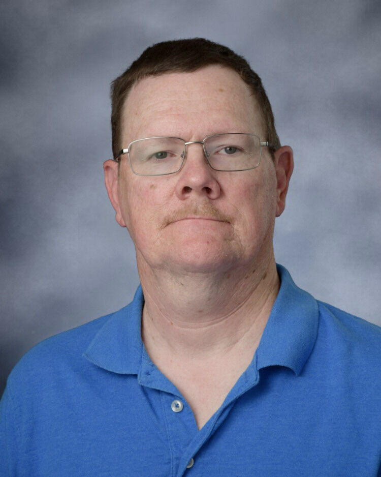 A middle-aged man with short brown hair and glasses poses against a studio background.