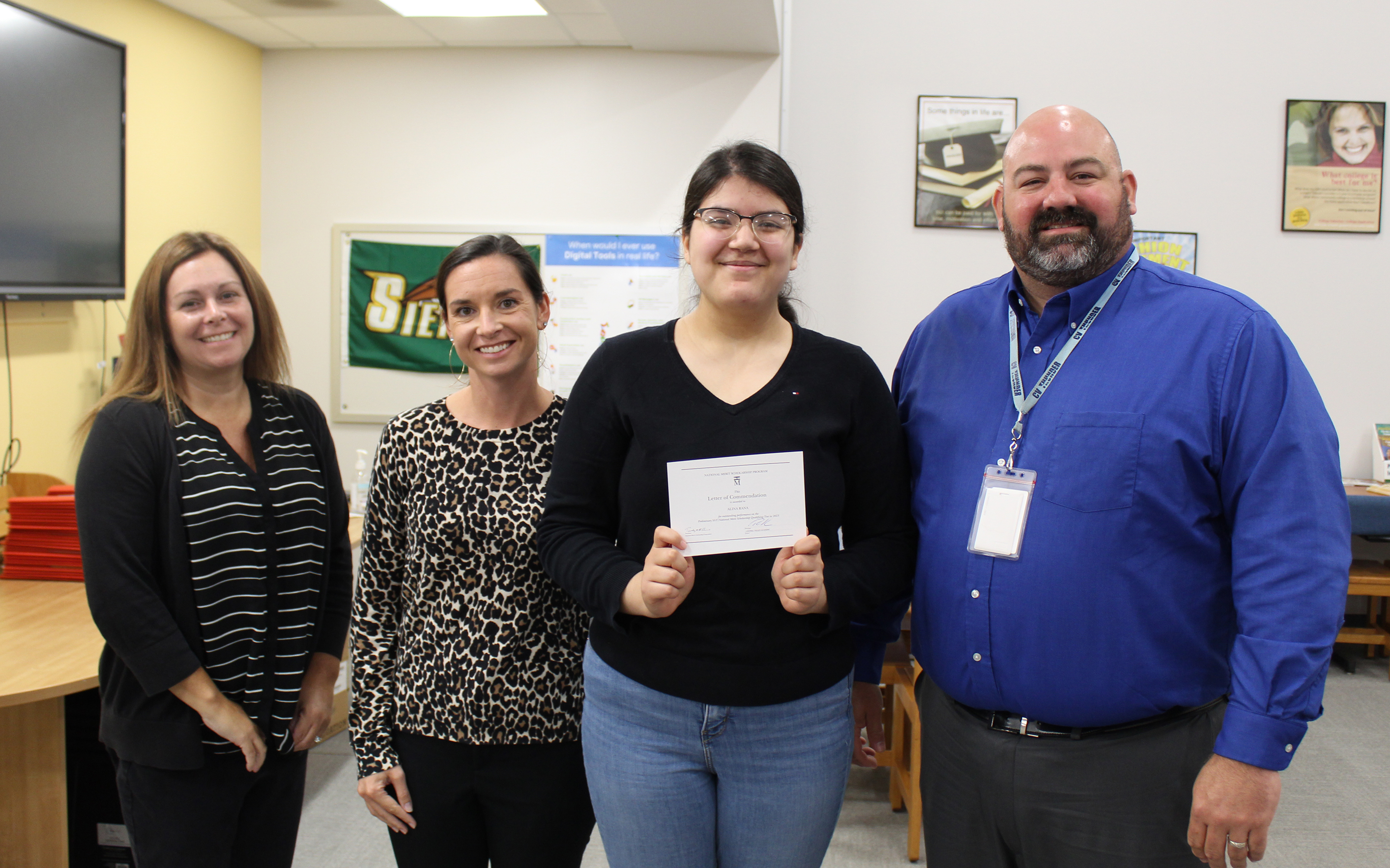 3 women and a man, standing and smiling in an office