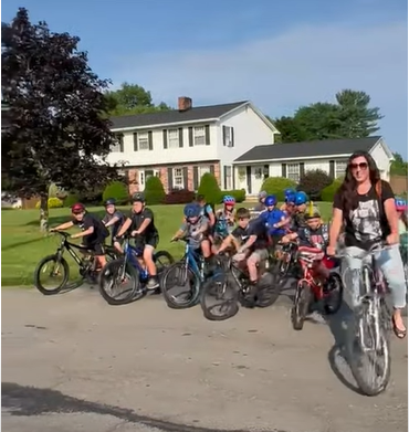large number of kids riding bicycles, house, trees, sky