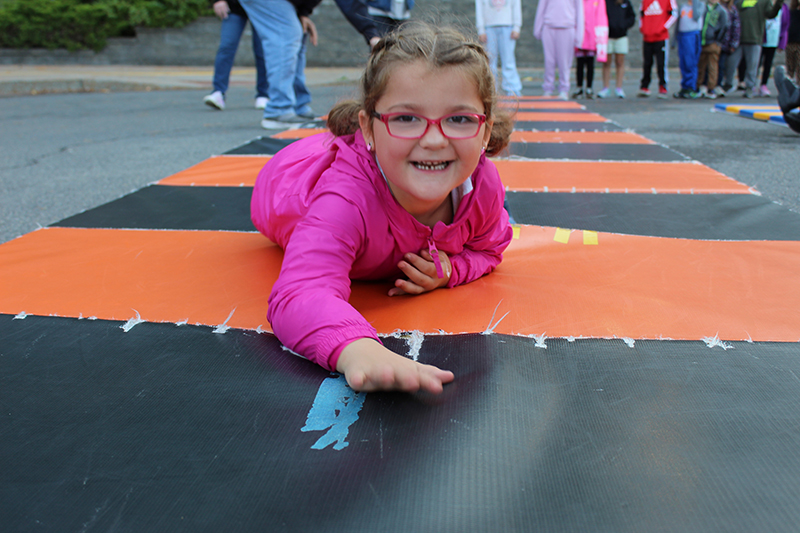 young girl crawling on elbows on mat, other students in background