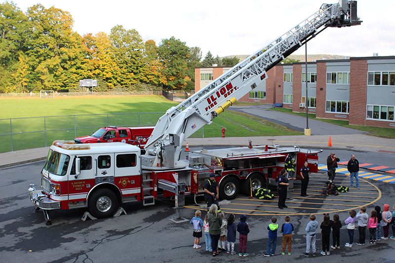 firetruck with ladder extended in parking lot by school, kids on sidewalk