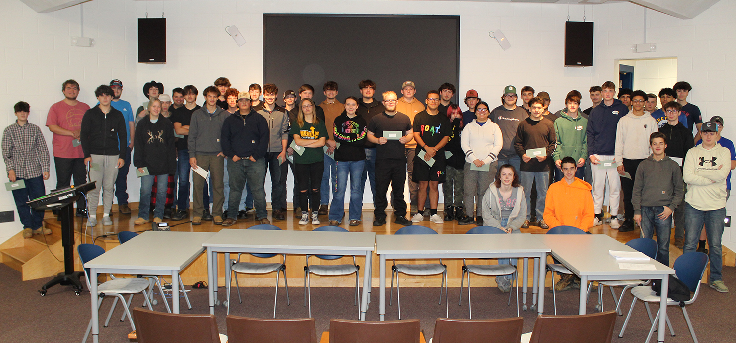 49 people standing in three rows on stage. table and chairs in the foreground