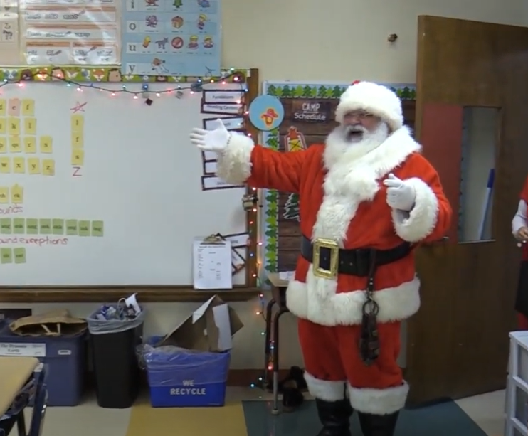 Santa with arms outstretched, walking into a classroom