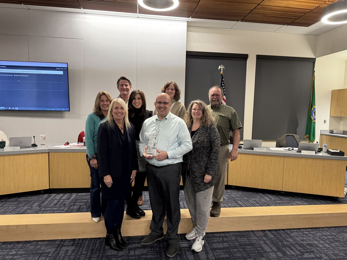 Three men stand on a stage, one speaking at a podium with the words 'Advocacy & Equity Institute' displayed behind him.