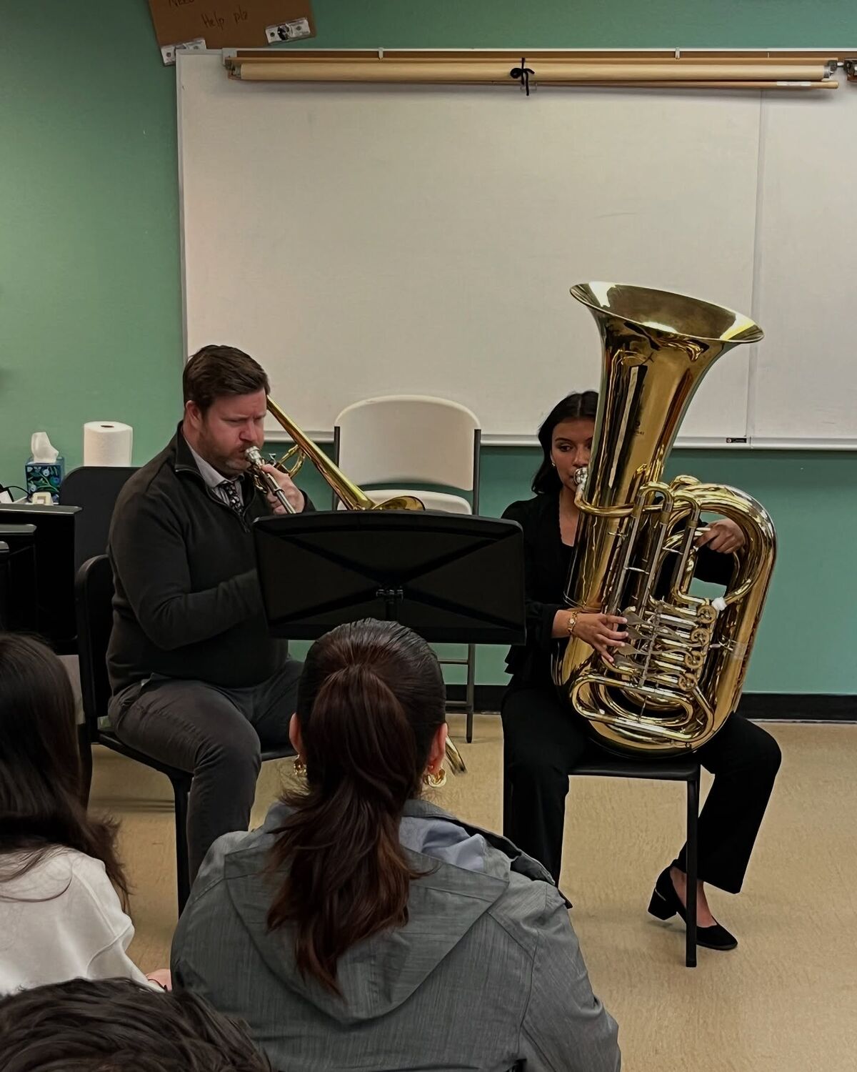 A man plays the trombone while a woman plays the tuba in front of an audience.