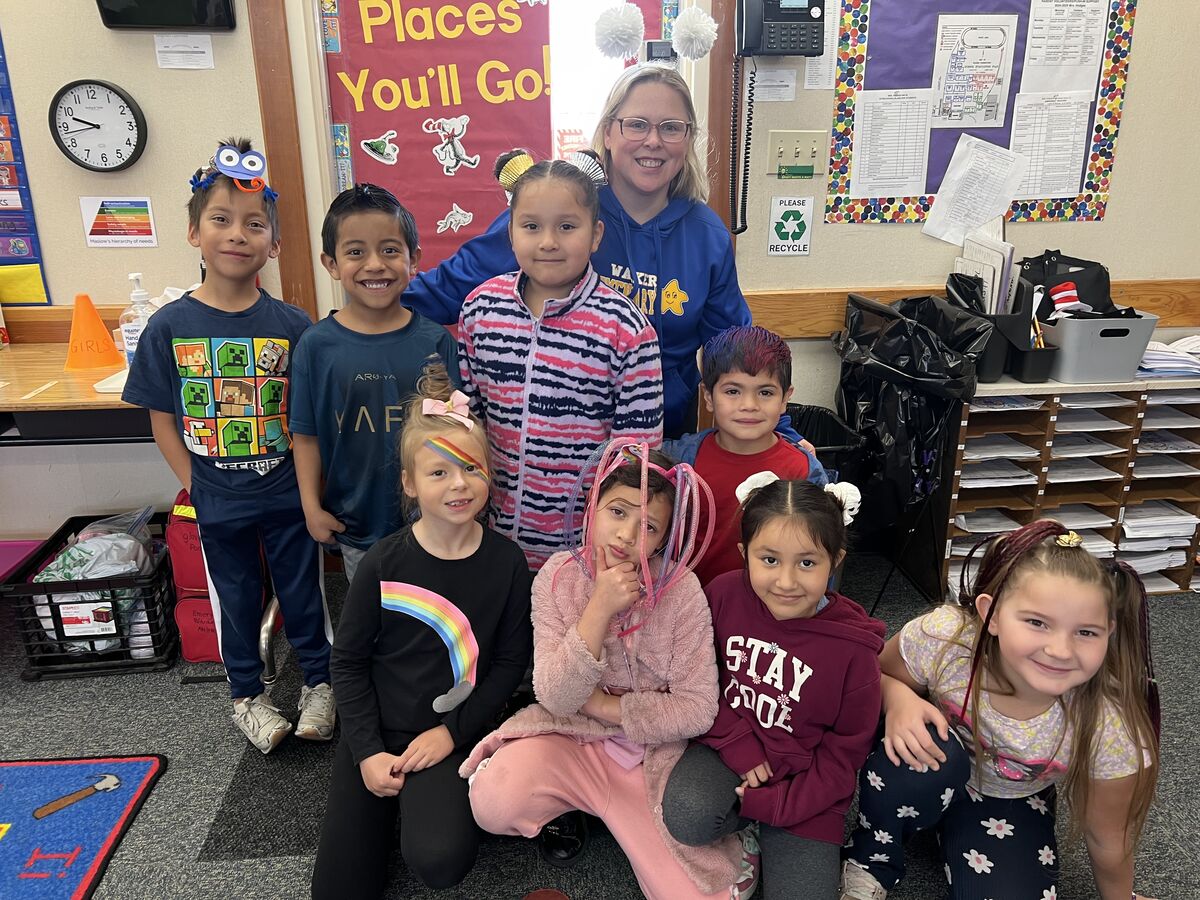 A group of elementary school students pose for a photo with their teacher, all wearing creative and colorful hairstyles.