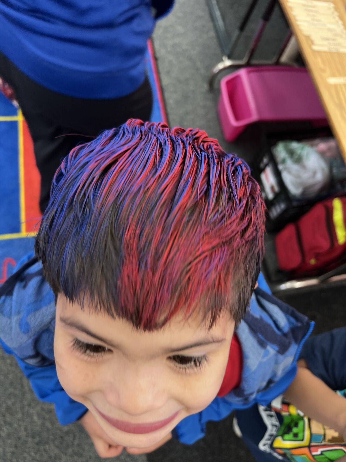 A young person with blue and red streaks in their hair smiles up at the camera.