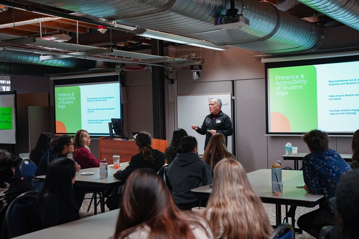 a presenter stands in front of a room full of students who are sitting at tables