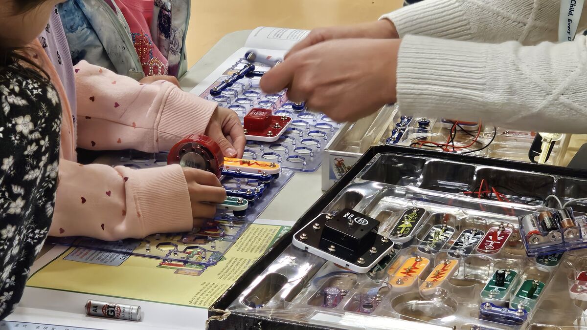 A child builds a circuit with colorful electronic components, guided by an adult.