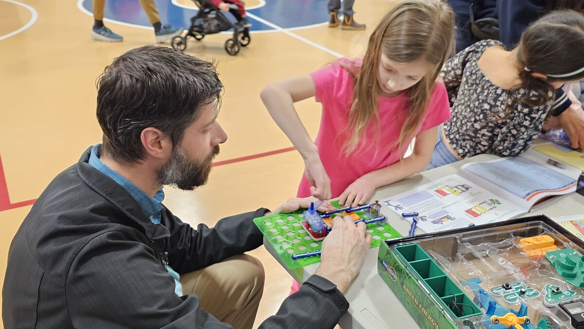 A man and a young girl work together on a science project, building a circuit with colorful wires and components.