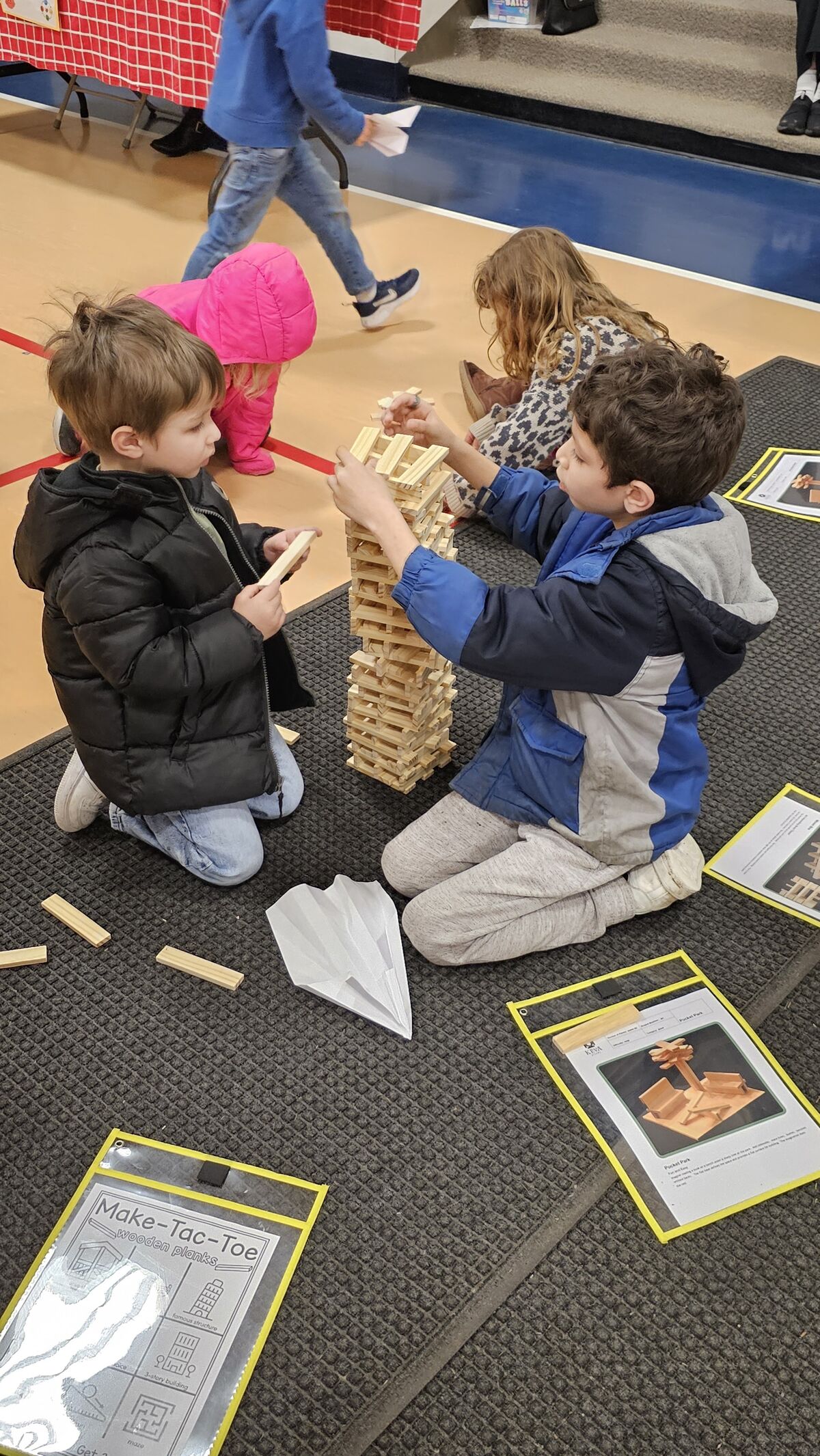 Children play a game with wooden blocks, building a tall tower.