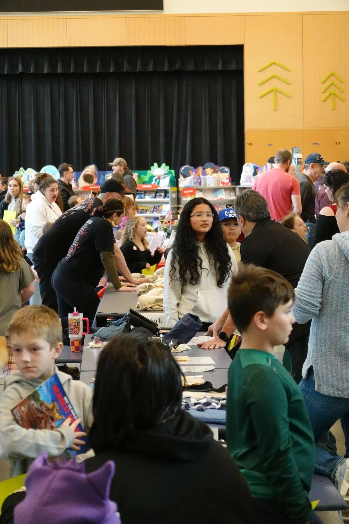 A group of people gather around tables, some looking at books and others talking.