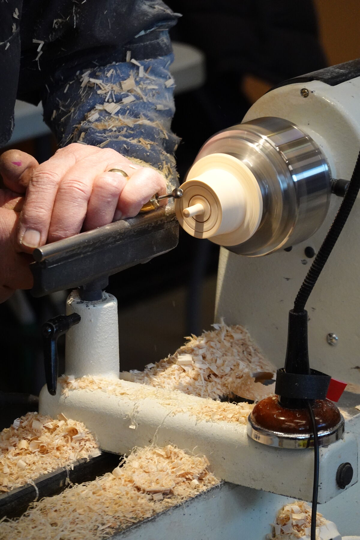 A woodworker uses a lathe to shape a piece of wood, creating wood shavings.