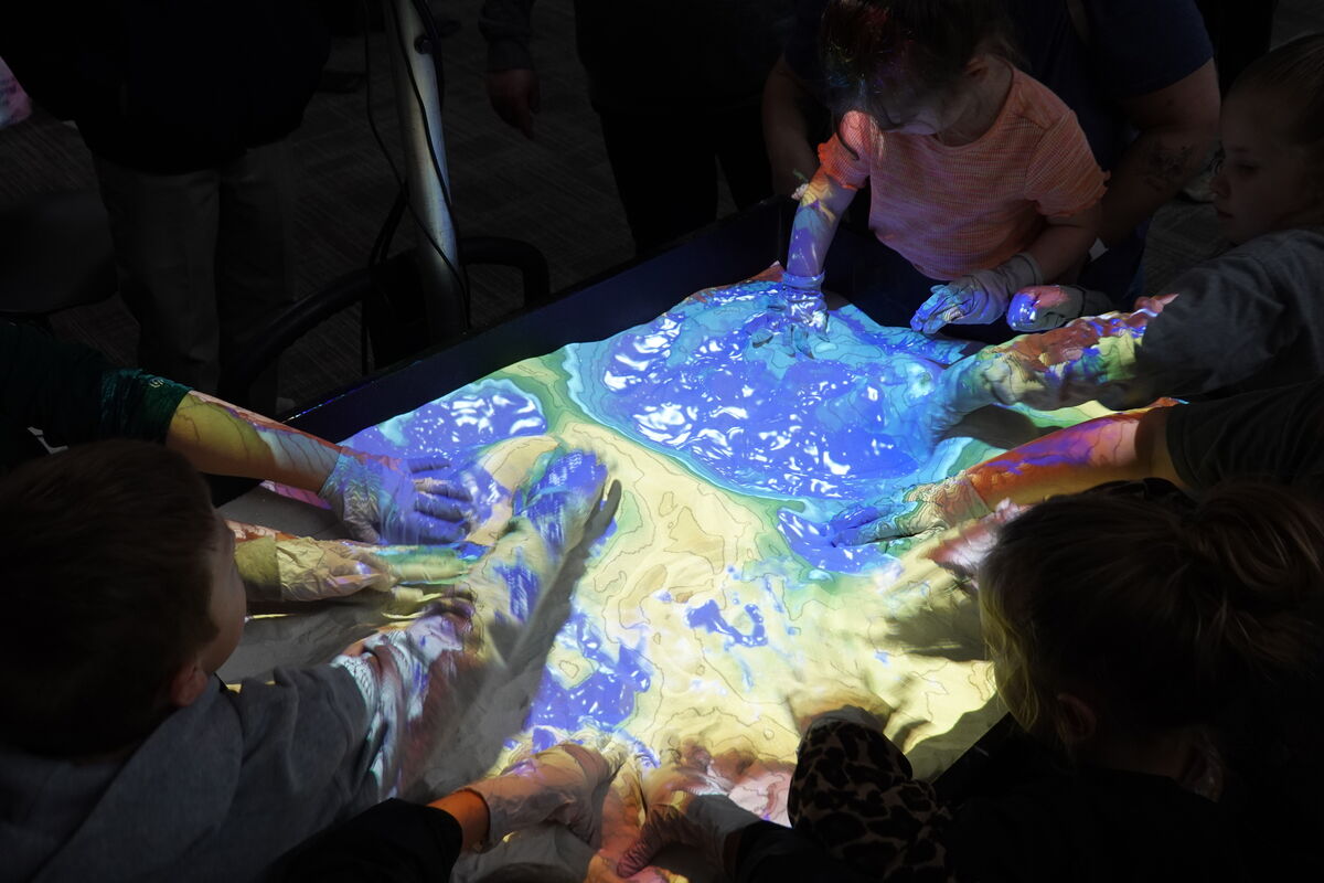Children interact with a projected map on a table, using their hands to explore the terrain.