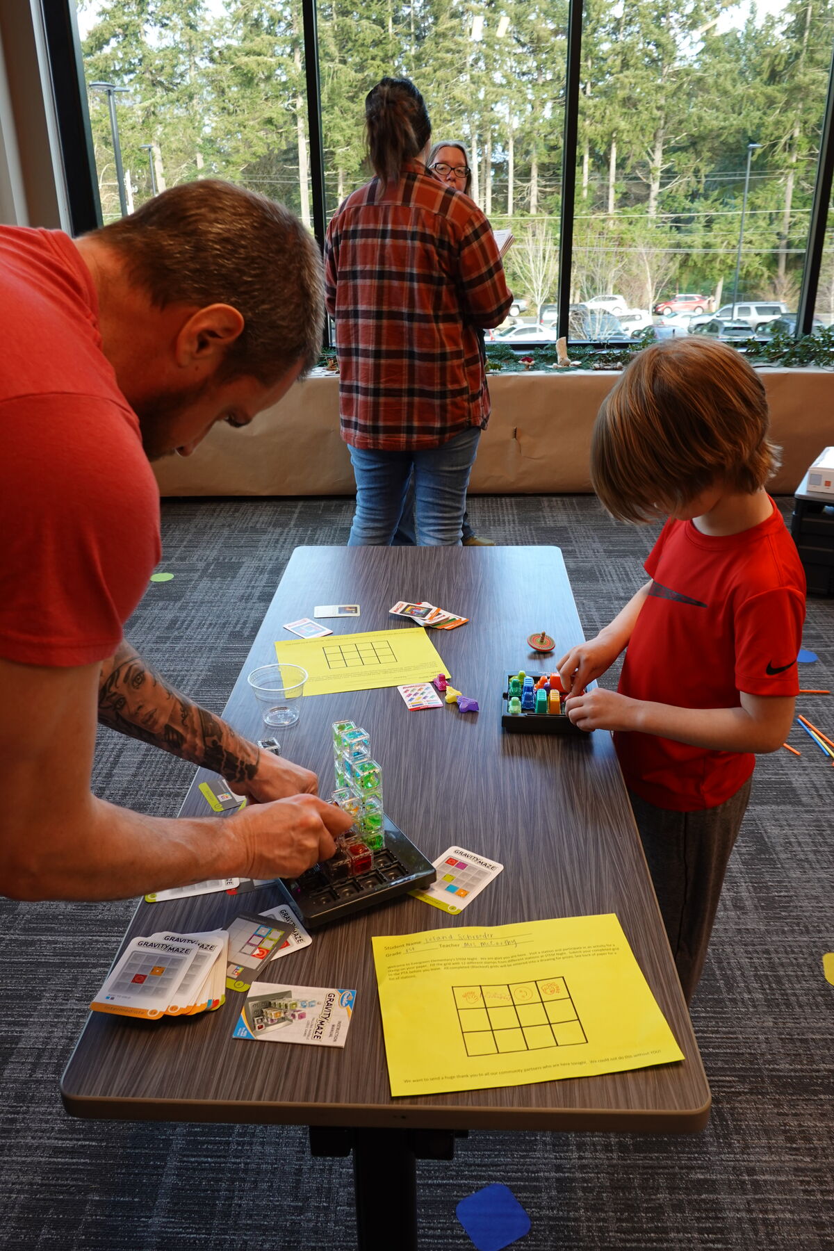 A young boy plays a game called Gravity Maze while an adult helps with the puzzle.