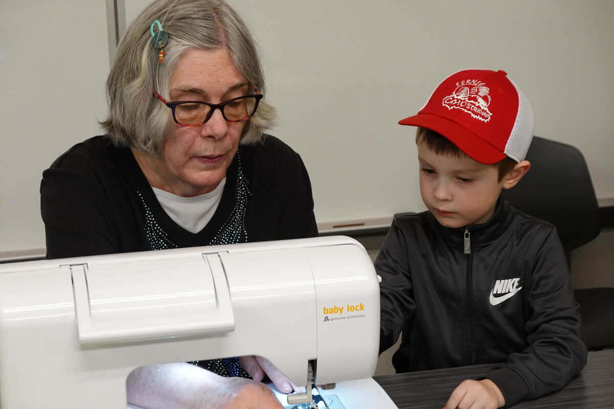 A woman teaches a young boy how to use a sewing machine.
