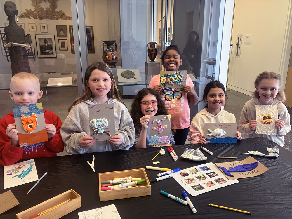 A group of children proudly display their art projects, which feature colorful animals and text like 'very cute' and 'calm strong'.