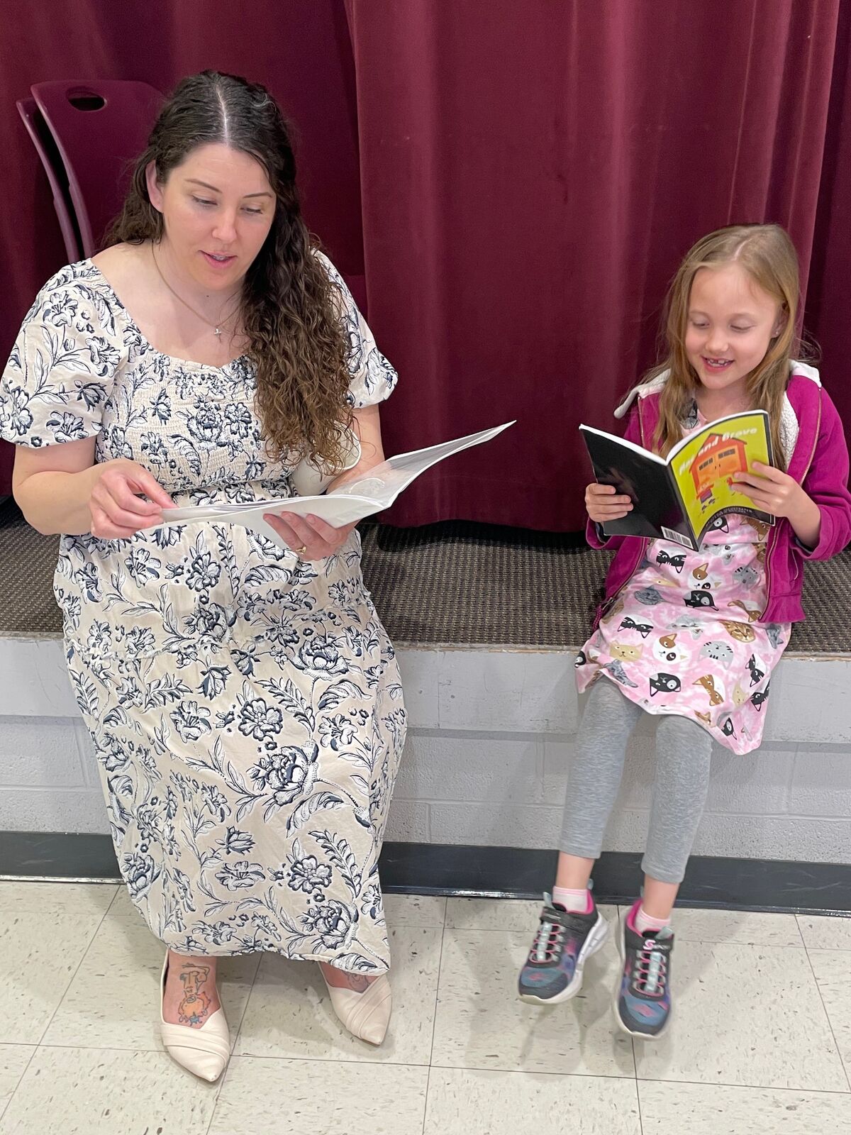 A woman and a young girl sit on a bench, both reading books.
