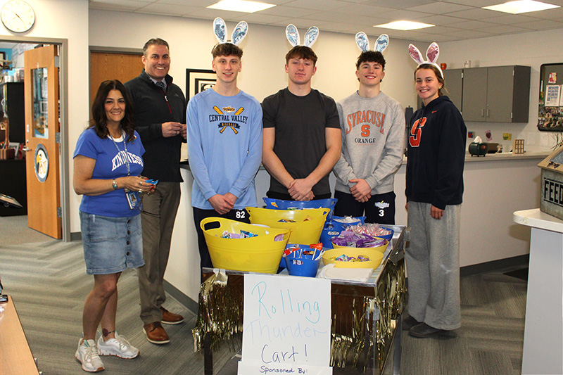 A group of students stand with a cart full of candy and snacks, wearing bunny ears.