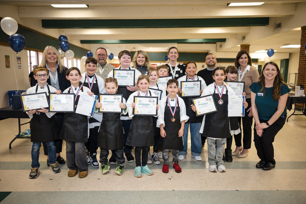 A group of young chefs stand proudly with their awards and certificates after a culinary competition.