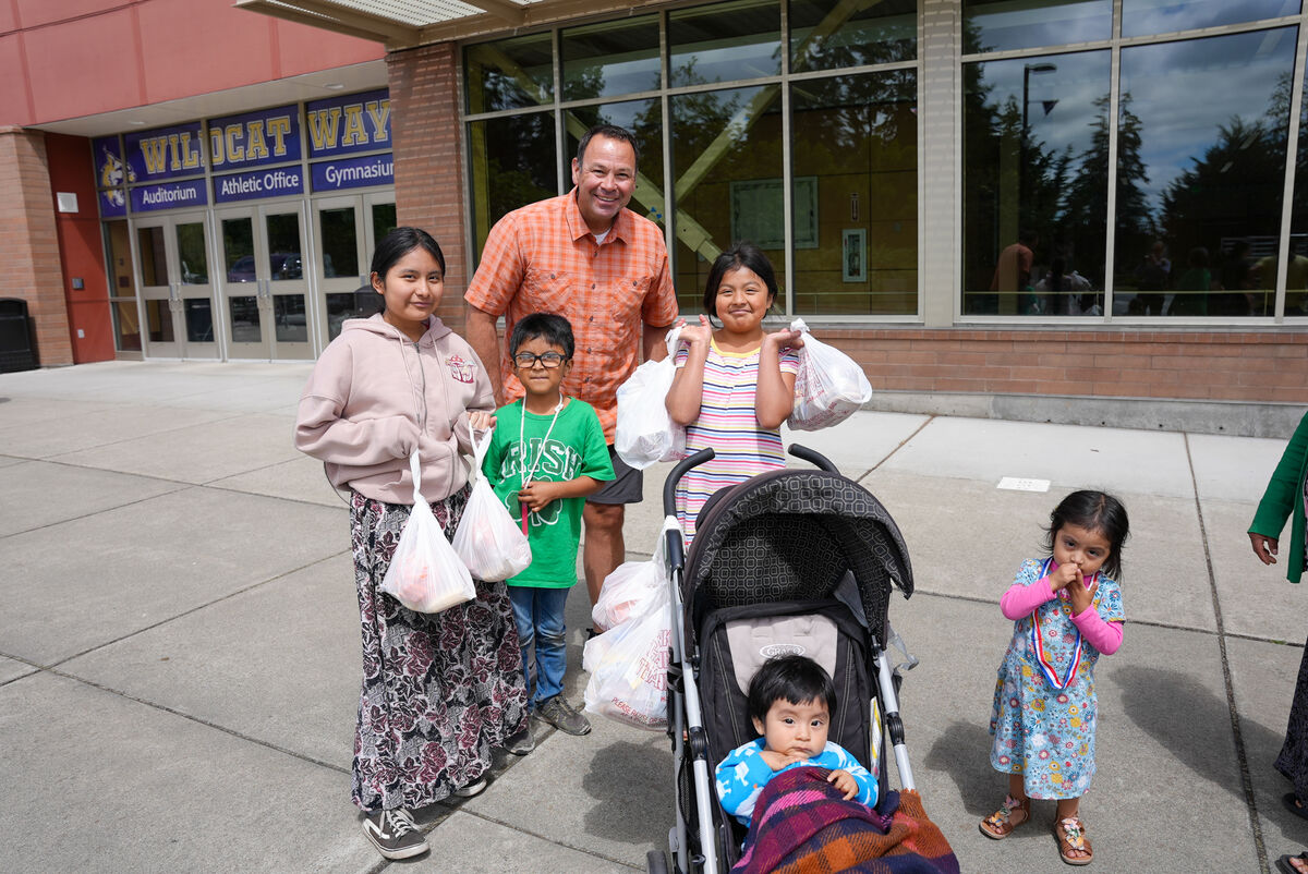 A group of people stand outside a school building, holding bags and smiling.