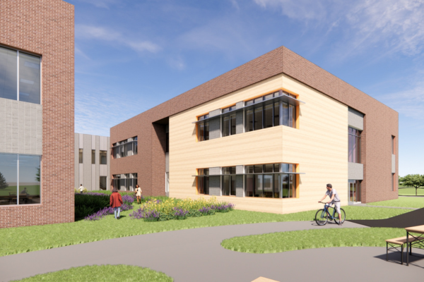 A modern school building with brick and wood siding, featuring large windows and a grassy courtyard with students walking and biking.