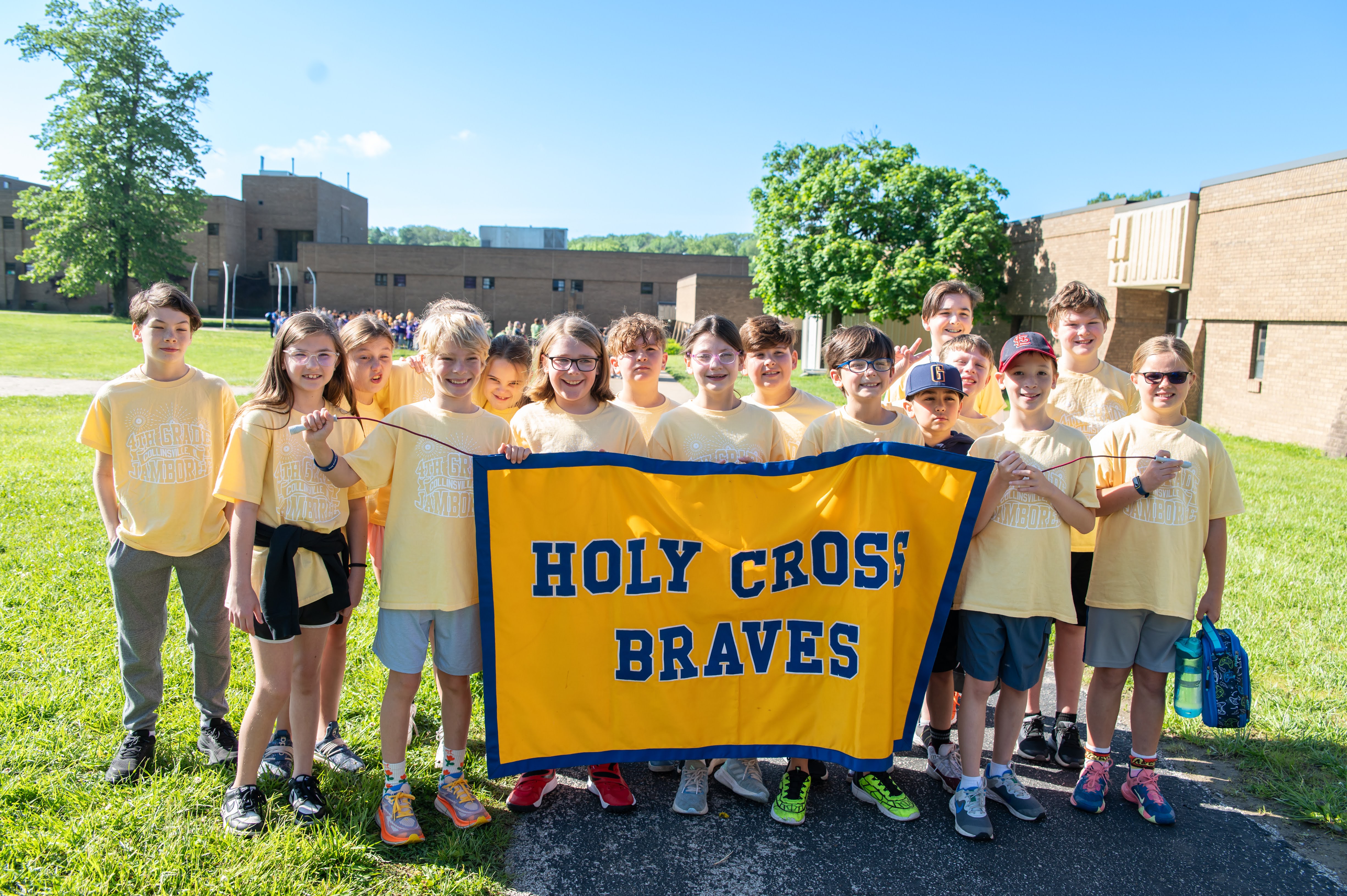 A group of students from Holy Cross hold a banner that reads 'HOLY CROSS BRAVES' while standing on a grassy field.