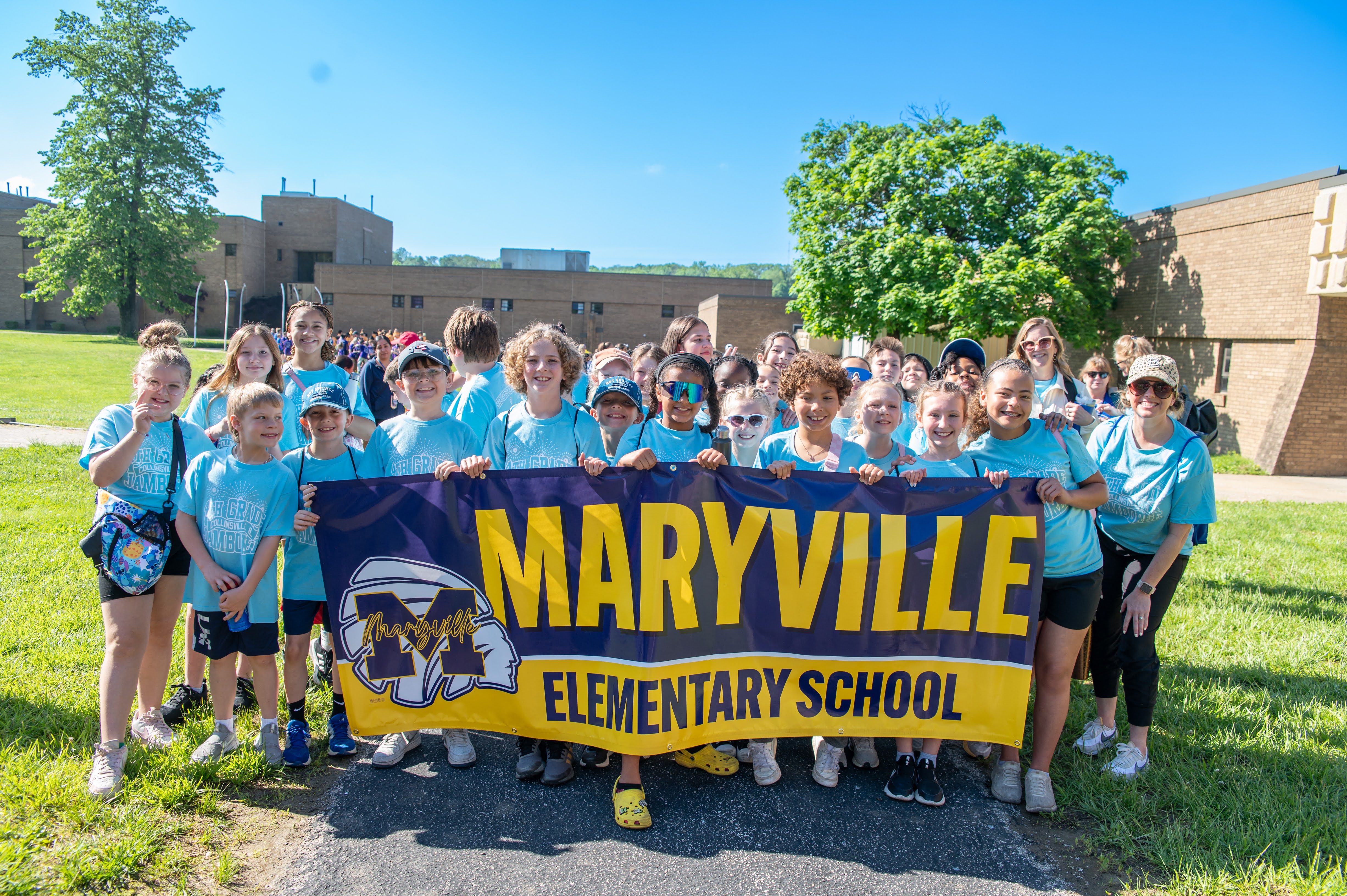 A group of children and adults hold a banner that reads 'Maryville Elementary School' in front of a school building.