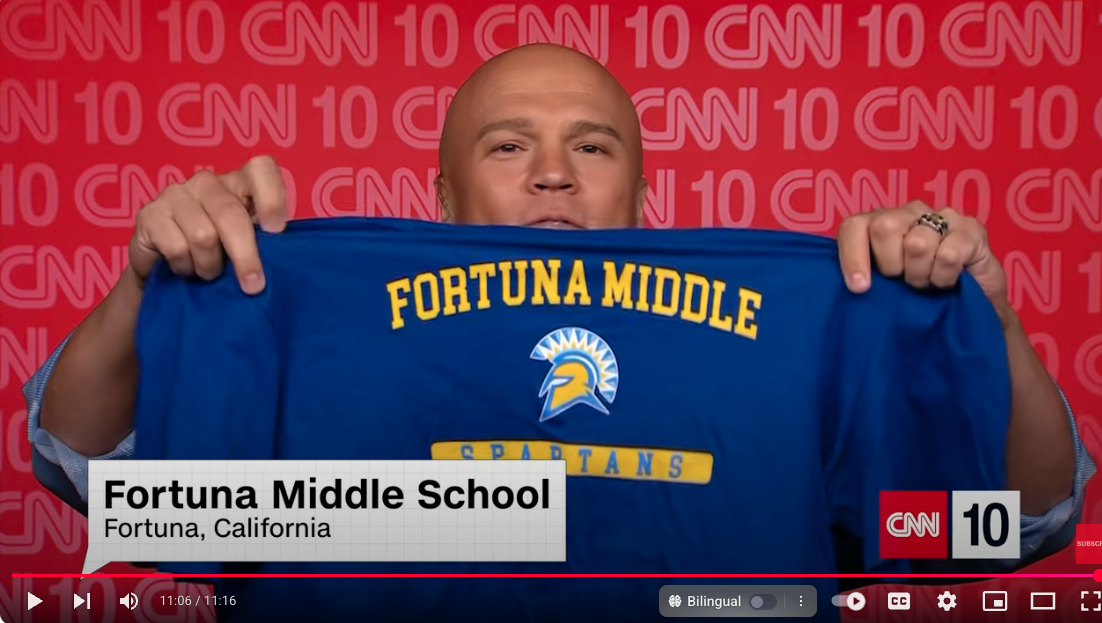 A man holds up a blue Fortuna Middle School shirt with the school's logo and mascot.