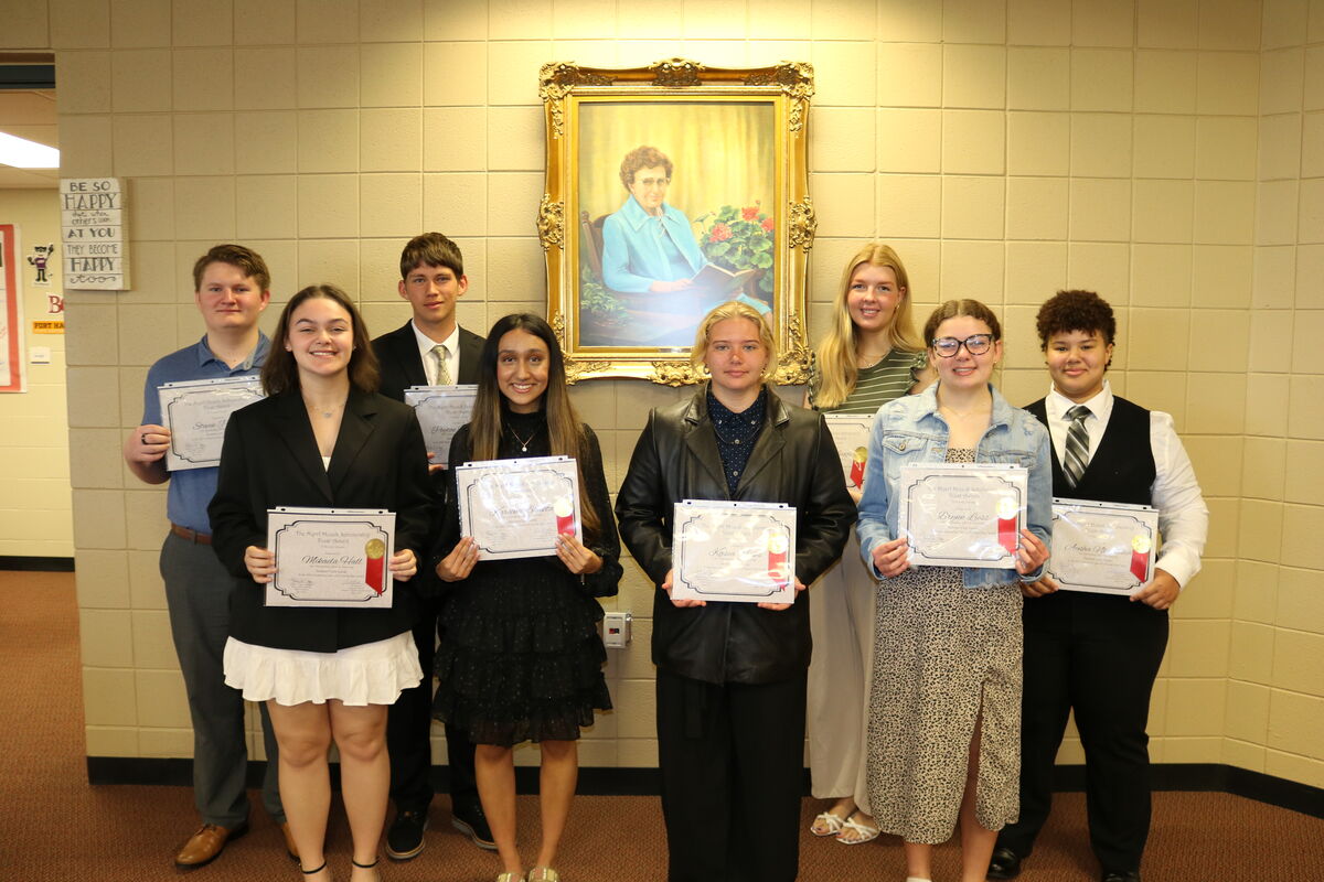 2025 Myrrl Houck Scholarship Winners pose with the former librarian’s portrait.
Front (L-R): Mikaela Hall, Kareena Bhakta, Kasea Hicks, and Brynn Liess 
Back (L-R): Steven Porter, Peyton Heilman, Sophia Beggs, and Aysha Nkrumbih
