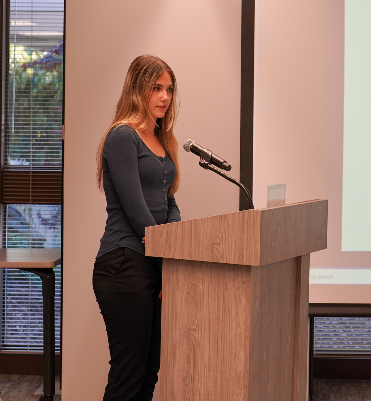 A young woman stands at a wooden podium, preparing to speak.