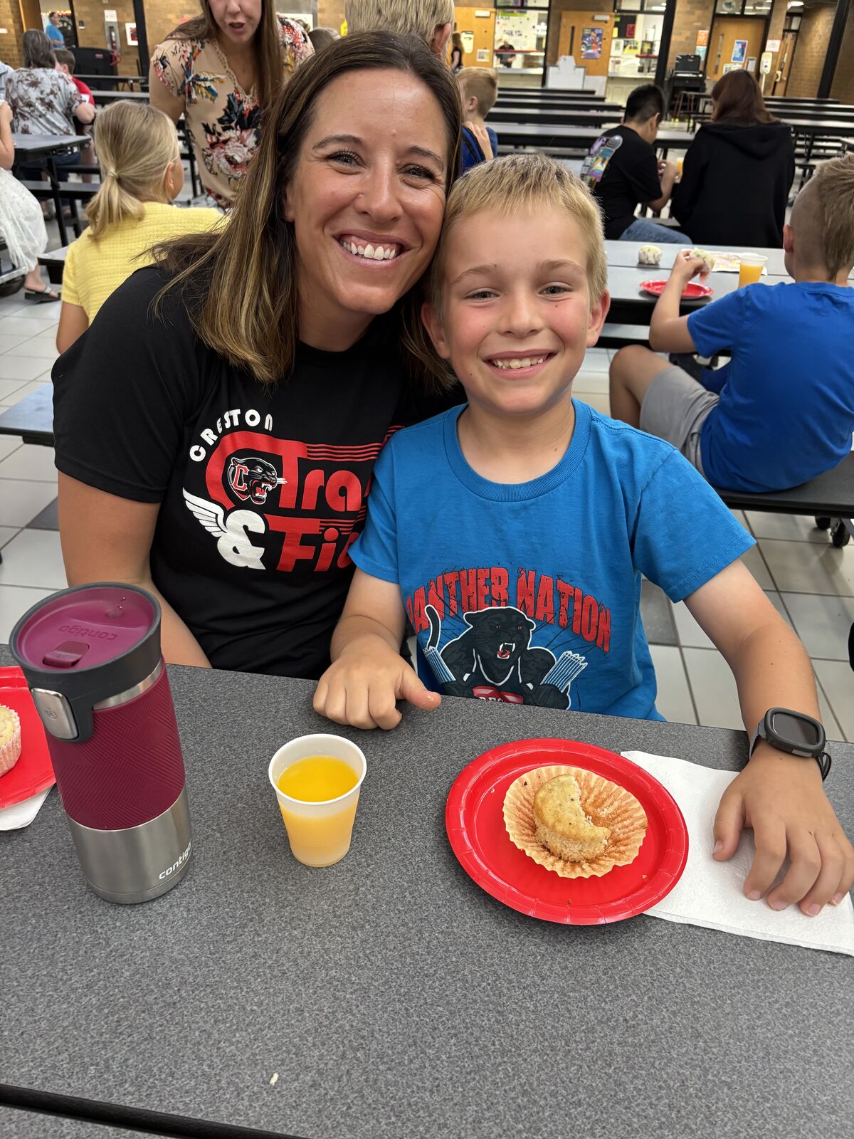 Elementary student and his mom pose together at a table, with food and drinks visible.