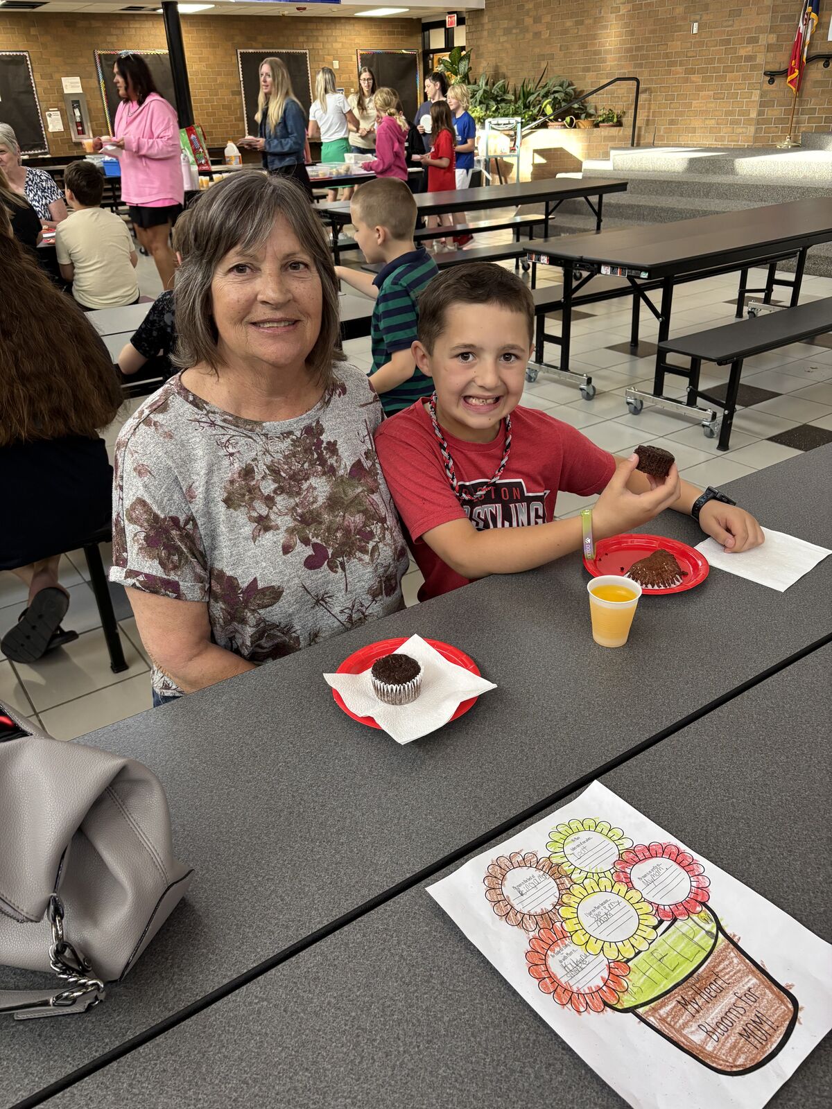 A smiling boy and woman sit at a table with treats and a drawing.